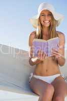 Happy blonde sitting on hammock holding book