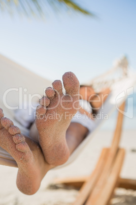 Close up of sandy feet of woman sleeping in a hammock
