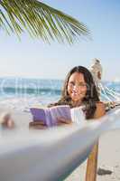 Woman lying on hammock holding book and smiling at camera