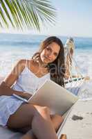 Brunette sitting on hammock with laptop smiling at camera