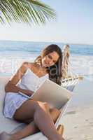 Brunette sitting on hammock using laptop