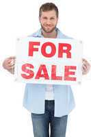 Charming young man holding a for sale sign
