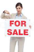 Estate agent holding and pointing to for sale sign