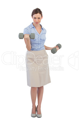 Tough businesswoman lifting dumbbells looking at camera