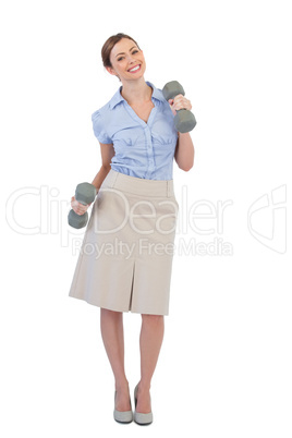 Happy businesswoman lifting dumbbells looking at camera