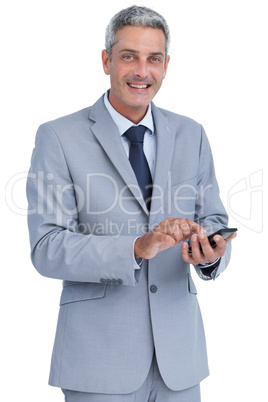 Cheerful businessman sending text message looking at camera