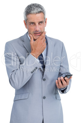 Thoughtful businessman touching his chin holding cellphone