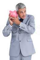 Doubtful businessman holding piggy bank