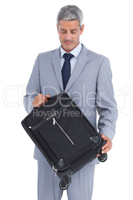 Handsome businessman carrying and looking at his suitcase