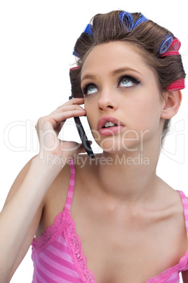Thoughtful young model wearing hair rollers with phone
