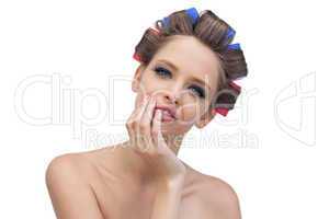 Cheerful model in hair curlers posing with hand on her face