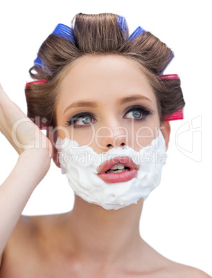 Thoughtful model in hair curlers with shaving foam posing