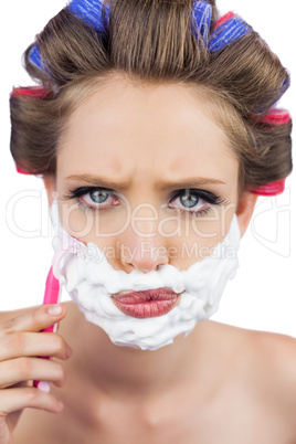 Serious model in hair curlers posing with shaving foam and razor