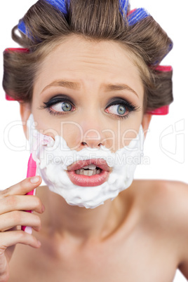Shocked young model in hair curlers posing with razor