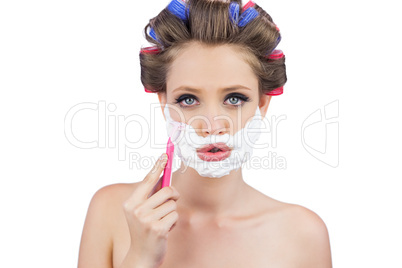 Young woman in hair curlers posing with razor