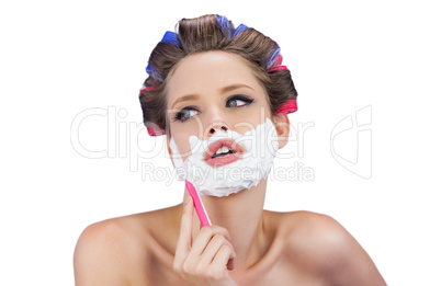 Pensive woman in hair curlers posing with razor