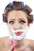 Curious model in hair curlers posing with shaving foam and razor