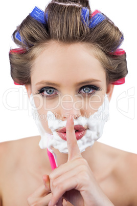Secretive woman in hair curlers posing with shaving foam and raz