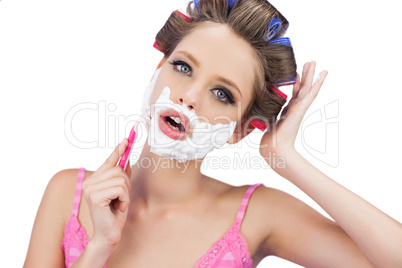 Model in hair curlers shaving her face