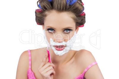 Serious model in hair curlers shaving her face