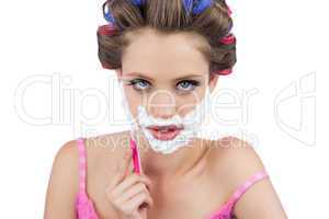 Serious model in hair curlers shaving her face