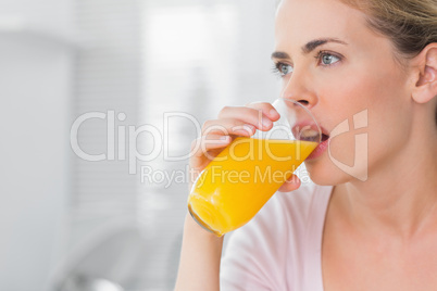 Thoughtful blond woman drinking orange juice