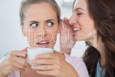 Smiling woman telling secret to her friend