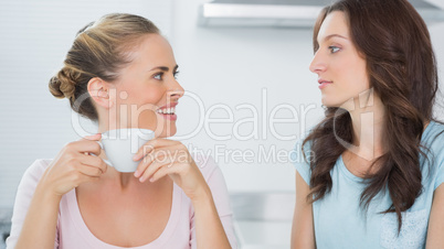 Smiling blonde looking at her friend and drinking coffee