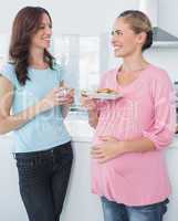 Smiling pregnant woman holding cookies and her friend