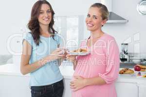 Smling pregnant woman holding cookies and her friend