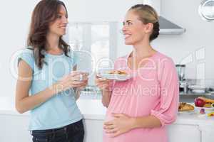 Happy pregnant woman holding cookies and her friend