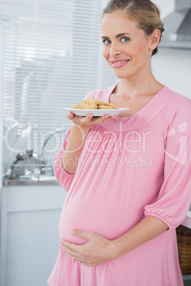 Happy expecting woman holding plate of biscuits