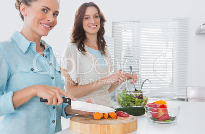 Woman cutting carrots with her friend mixing salad