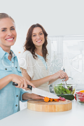 Women preparing a salad together smiling at camera