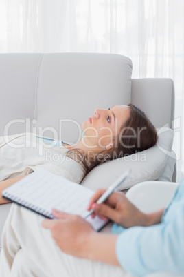 Worried woman lying on the couch while psychologist writing