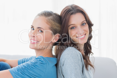 Cheerful women back against back and looking at camera
