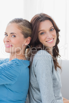 Happy women back against back and looking at camera