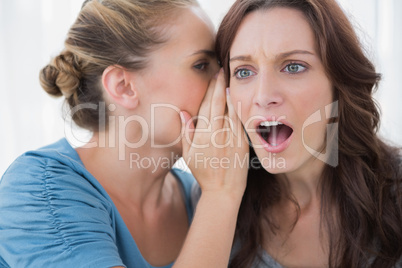 Stunned woman being told a secret by her friend