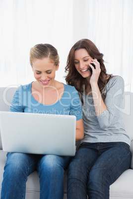 Blond woman using her laptop with her friend having a phone call