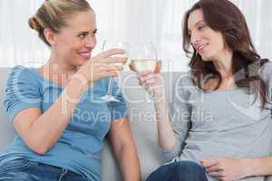 Happy women clinking their wine glasses while sitting on the sof