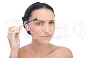 Frowning young brunette using eyebrow brush