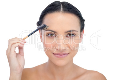 Peaceful young brunette using eyebrow brush