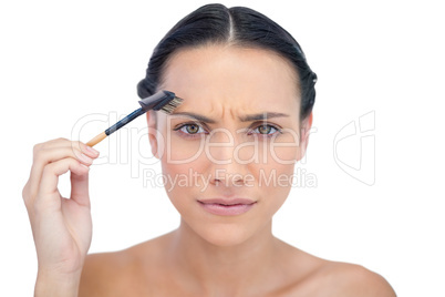 Unsmiling young brunette using eyebrow brush