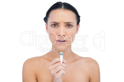 Frowning young brunette holding nail clippers