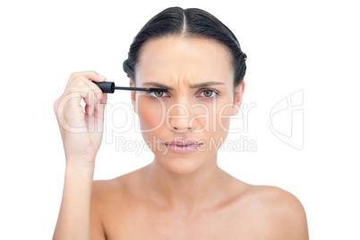 Frowning young brunette applying mascara