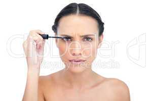 Frowning young brunette applying mascara