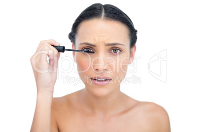 Annoyed young brunette applying mascara