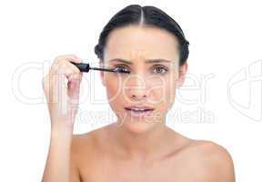 Annoyed young brunette applying mascara