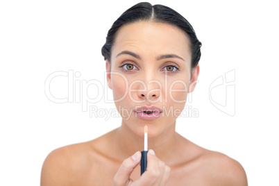 Young model applying lip gloss while looking at camera