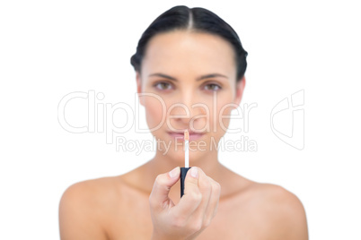 Young model holding lip gloss while looking at camera